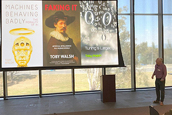 A man stands in front of a large projector screen showing images of different AI-related books.